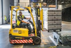 A warehouse worker maneuvers a forklift to transport crates for brewing company storage.