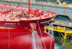Red ship named 'SPIRIT II' in dry dock with cranes and industrial backdrop.